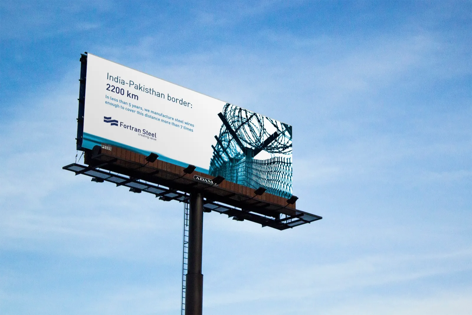 Billboard against a blue sky carrying the Fortran Steel campaign ad about the 2,200 km India–Pakistan border, with copy about the company’s steel wire capacity.