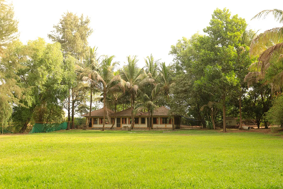 Wide daylight photograph of the resort grounds: a large open lawn in front of a single-storey tiled-roof pavilion surrounded by trees.