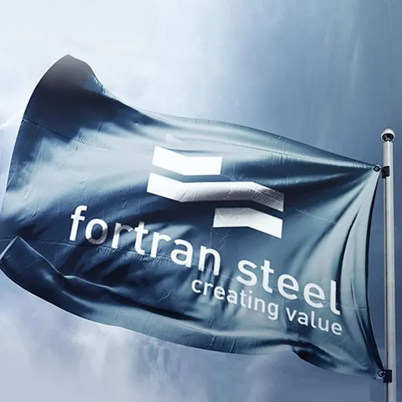 Slate-blue Fortran Steel flag on a flagpole against a stormy sky, with the chevron mark and the line “creating value”.
